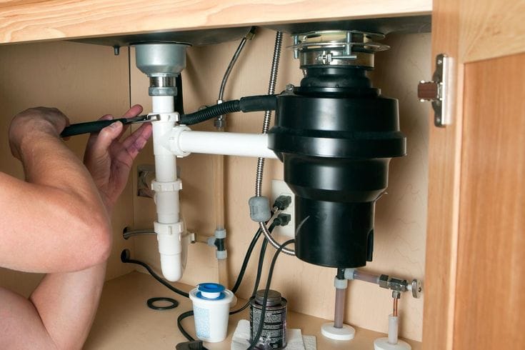 Plumber installing a garbage disposal beneath a kitchen sink in Dunedin